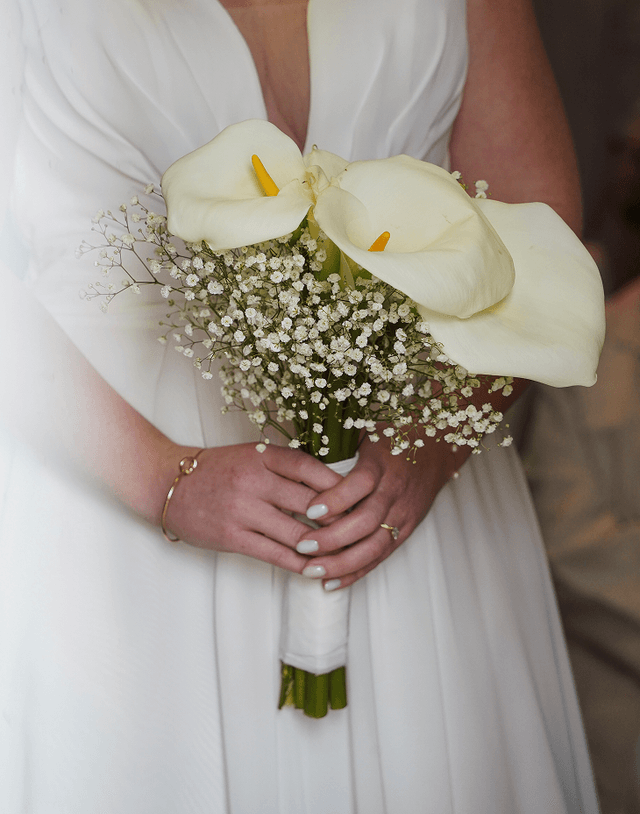 Mariée tenant un bouquet de callas blancs et de gypsophile.